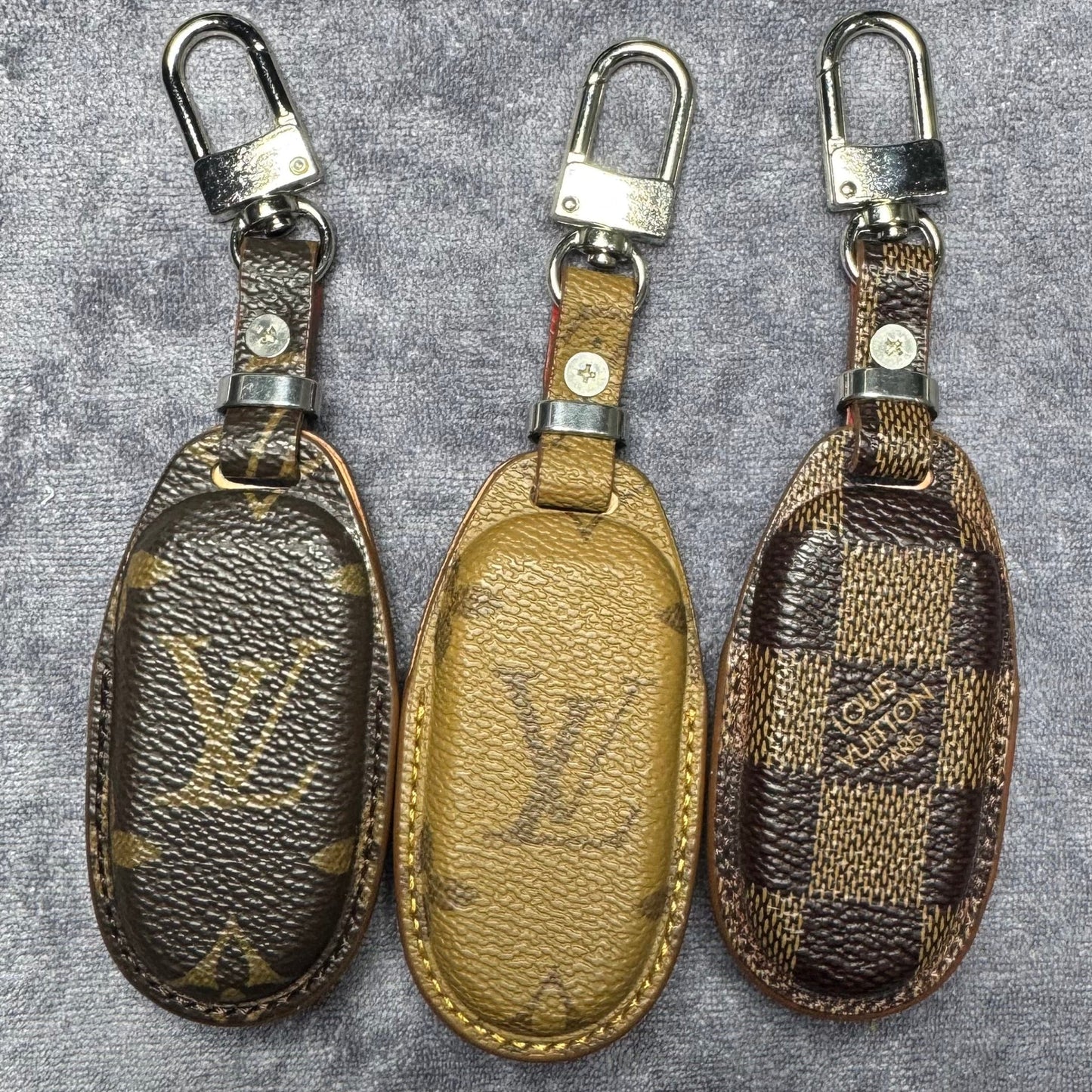 Three Louis Vuitton keychains on a textured gray background