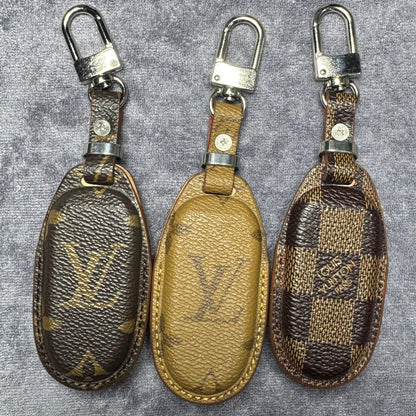 Three Louis Vuitton keychains on a textured gray background